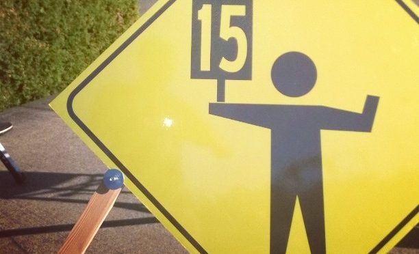 A man holding a 15 sign on a pedestrian crossing sign