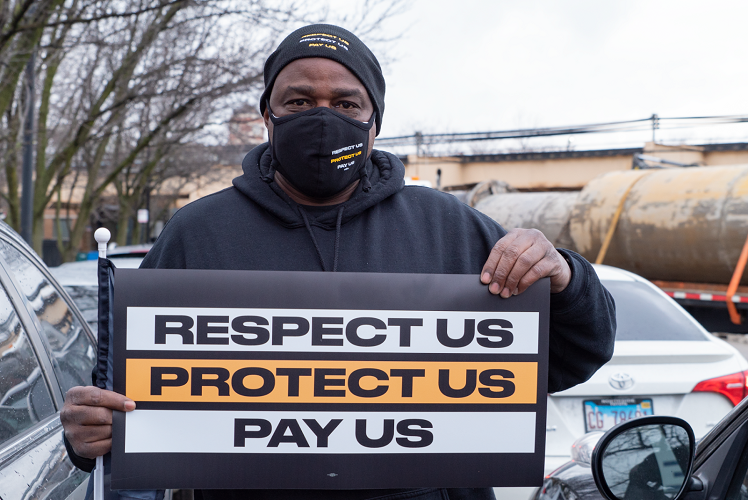 Man holding sign that says "Respect Us. Protect Us. Pay Us."