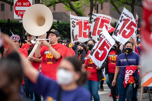 A brass band and group of workers marching with Fight for $15 signs.
