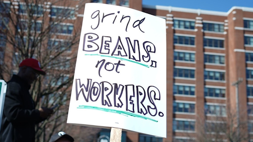 A protest sign reading "Grind Beans, Not Workers"